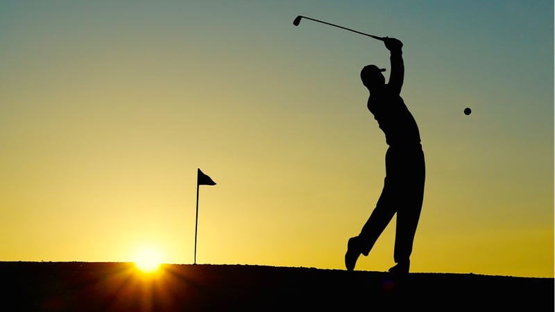 Golfer beim Abschlag vor der aufgehenden Sonne.